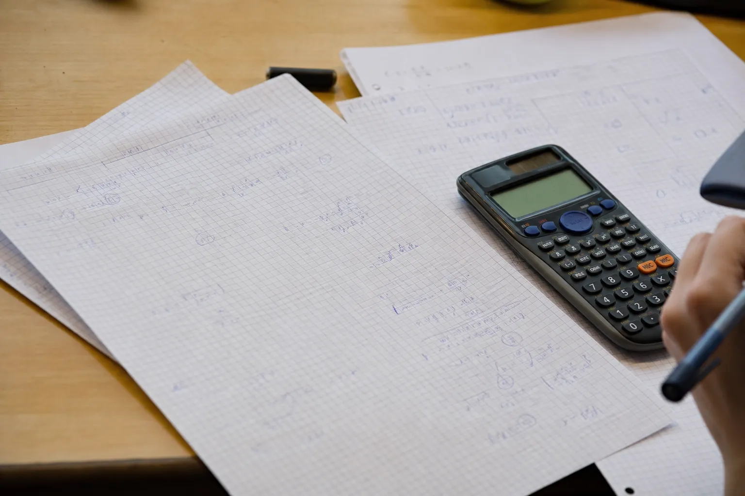 Feuilles de calcul manuscrites et une calculatrice posées sur un bureau