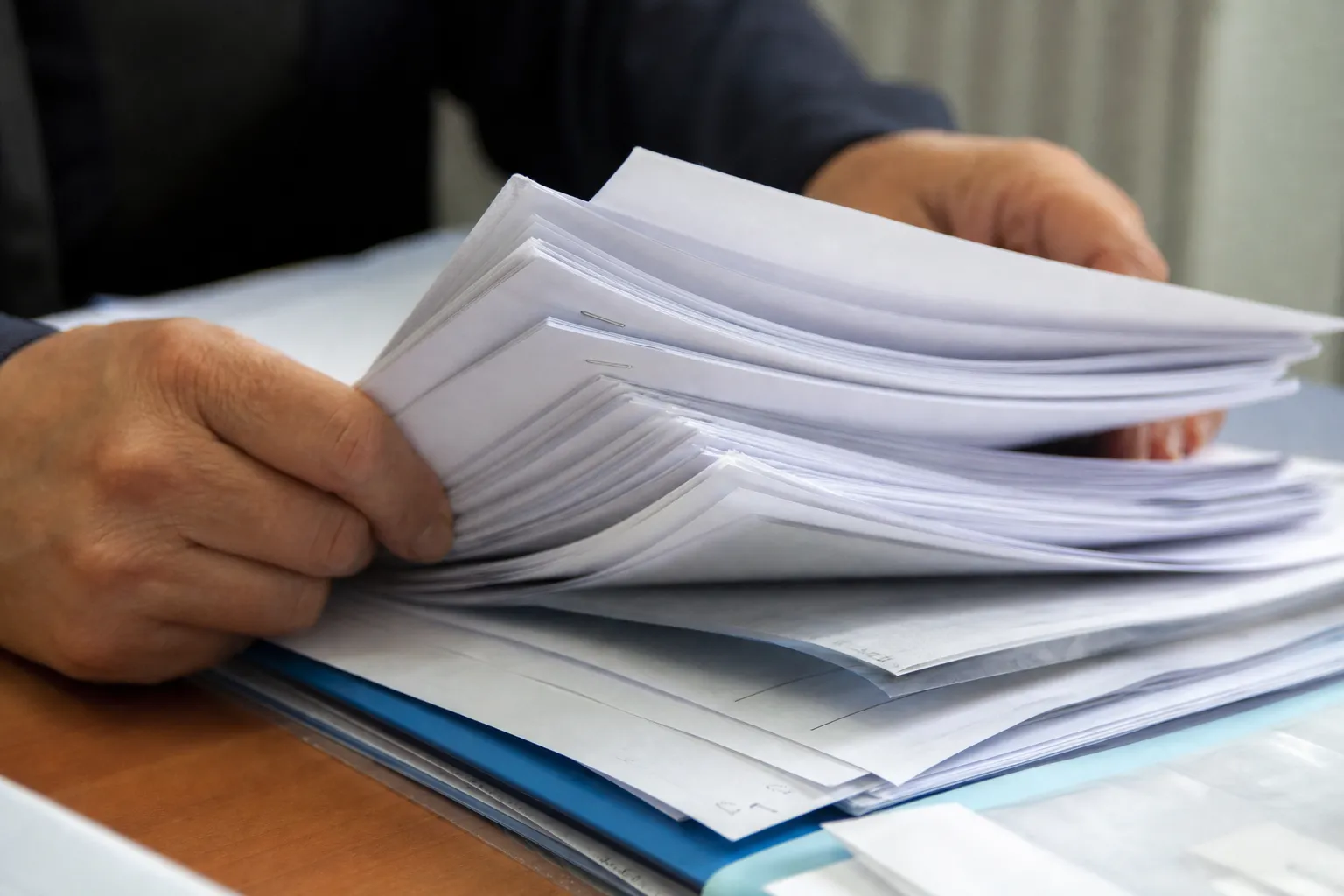 Mains qui feuillettent un dossier papier rempli de feuillets agrafés