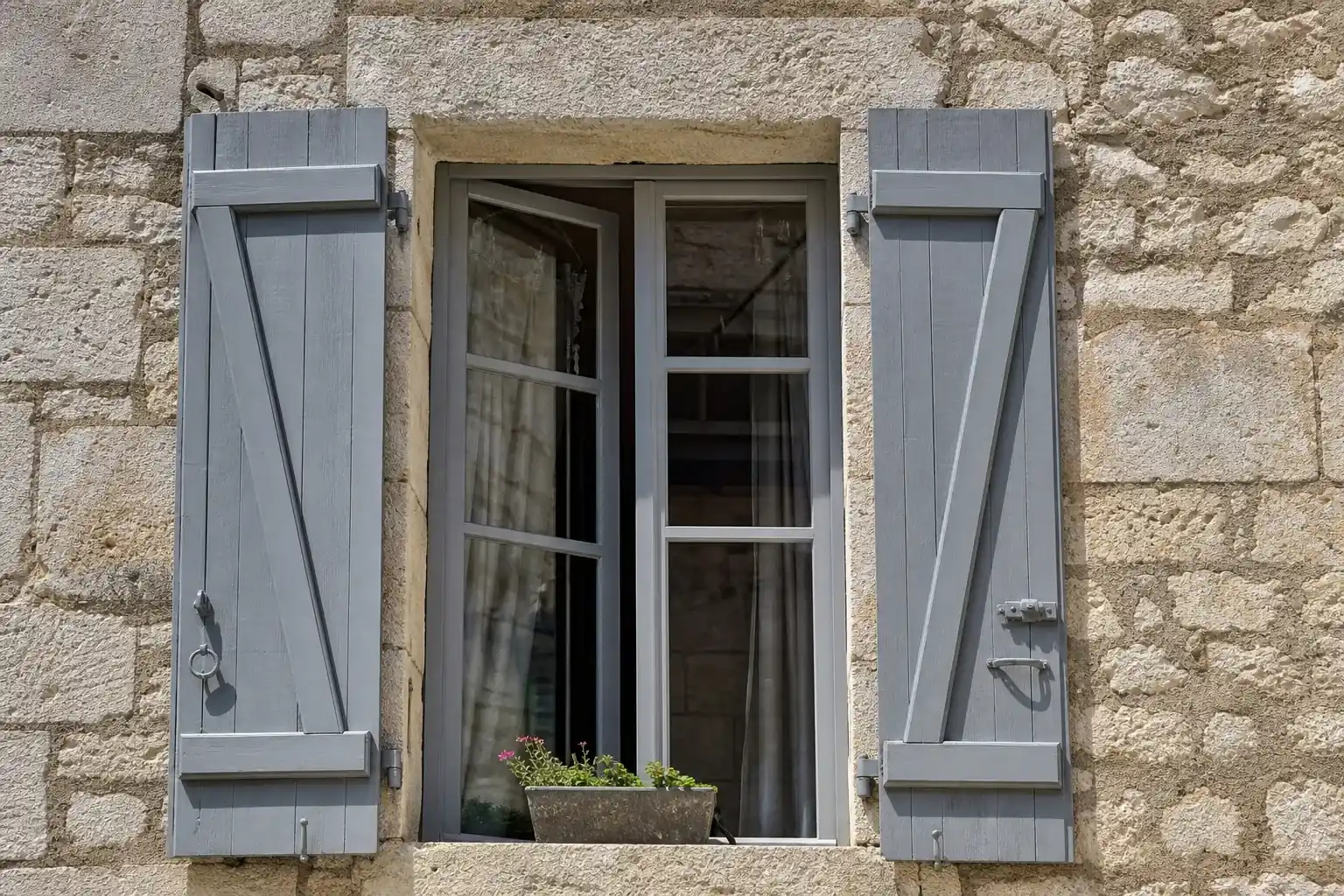 Fenêtre entrouverte avec volets en bois peint sur une façade en pierre de taille